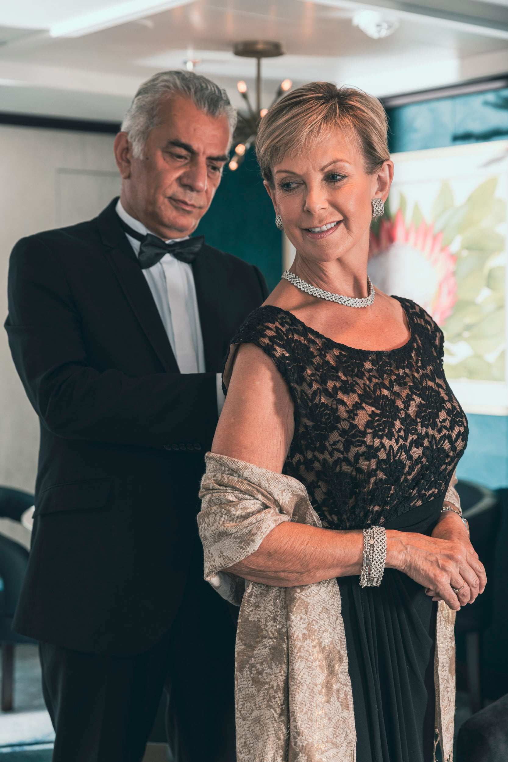 Saga cruise evening photography — couple in black-tie attire dressing for a formal night, woman in a black lace gown