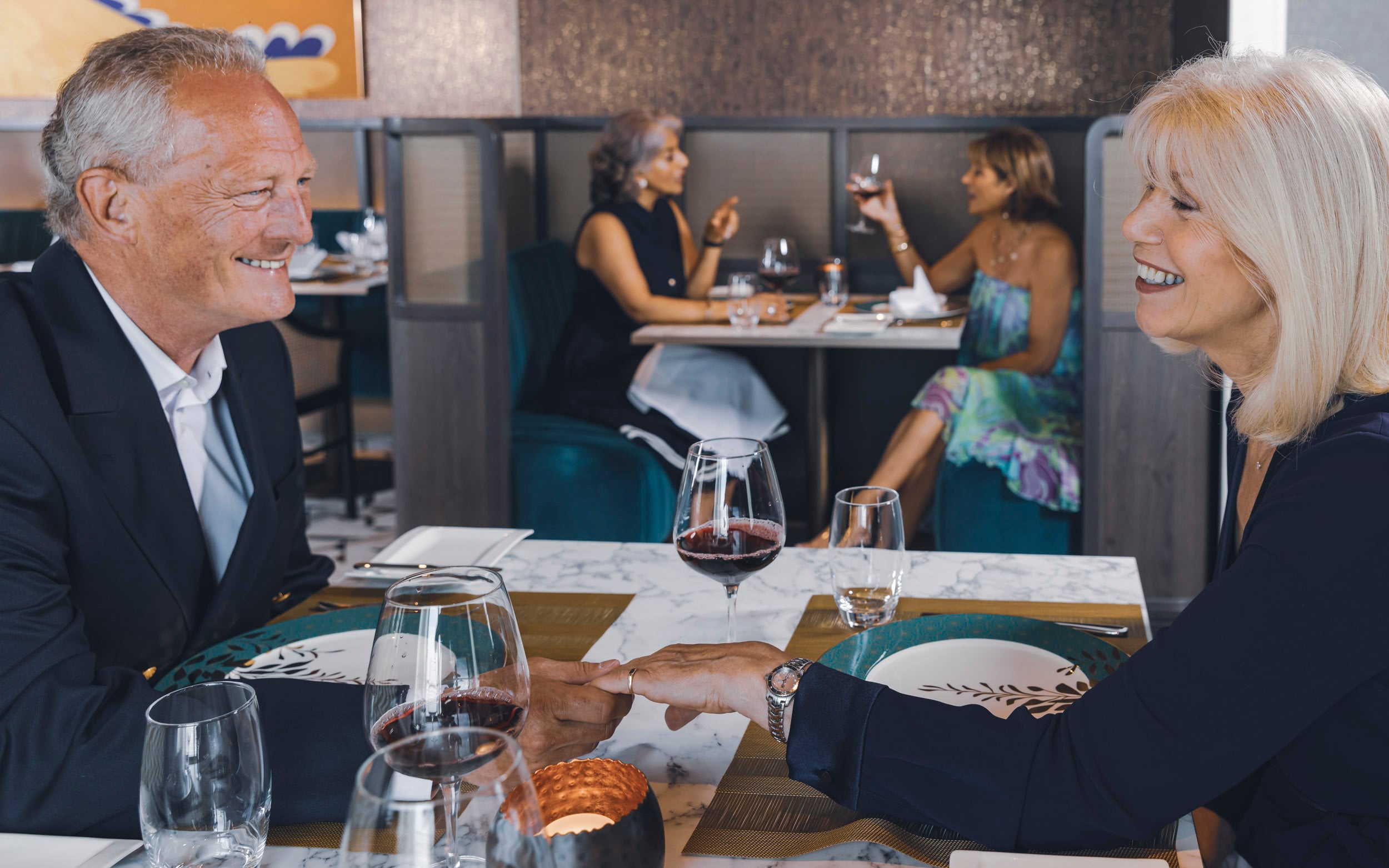 Saga cruise dining photography — couple holding hands across a candlelit dinner table, fellow guests behind