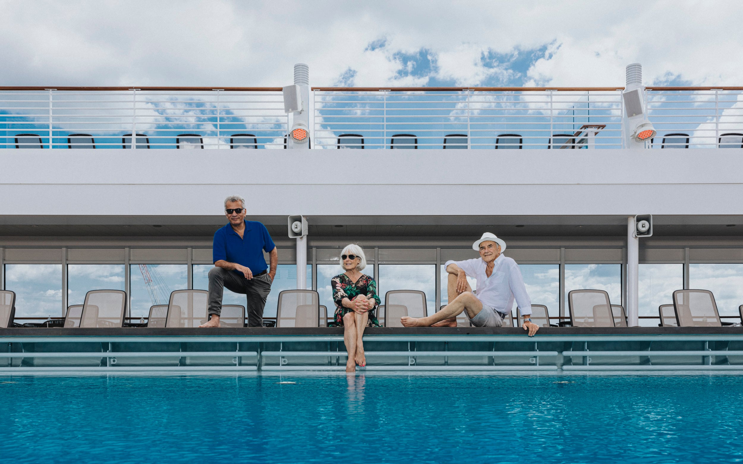 Saga cruise lifestyle photography — three guests by the outdoor swimming pool on a sun-drenched deck