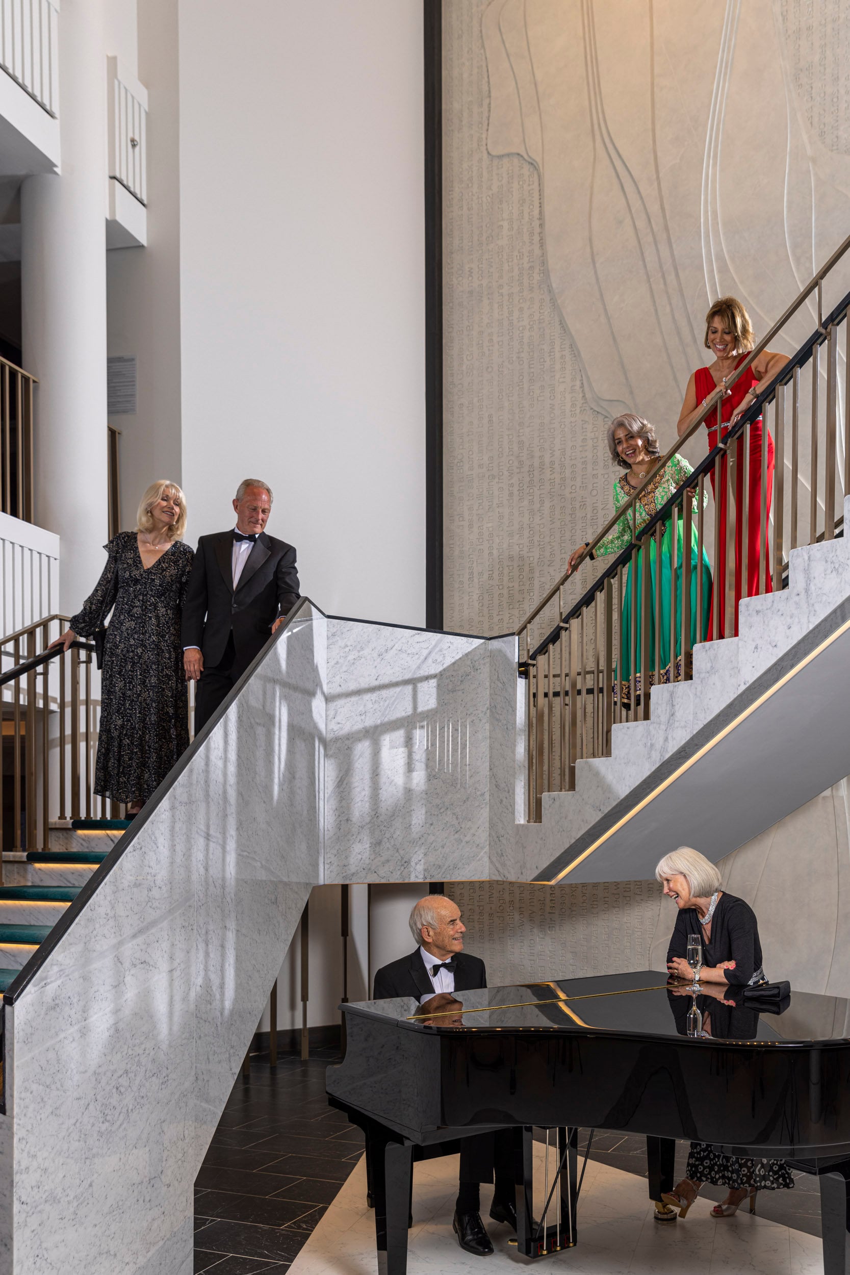 Saga cruise atrium photography — guests in evening wear on the grand staircase with a pianist at the marble foot