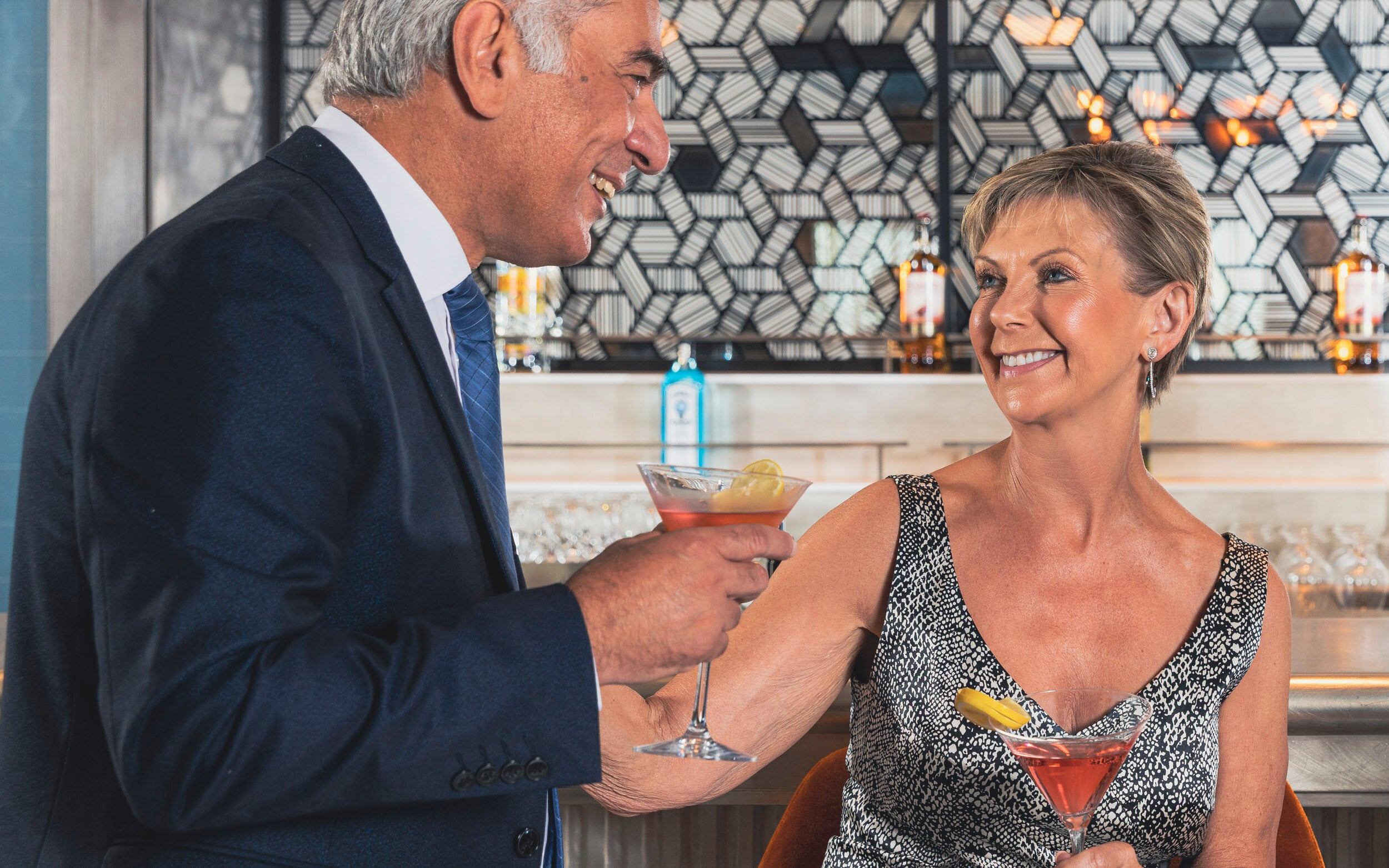 Saga cruise cocktail-bar photography — couple in evening wear toasting martini cocktails at the bar