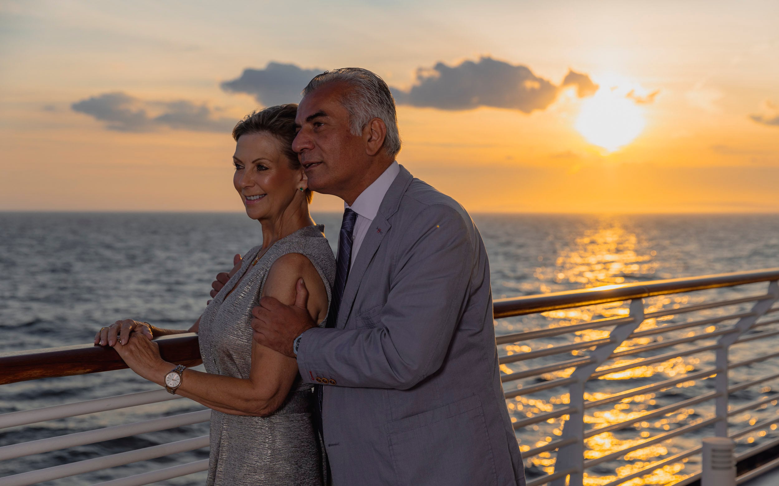 Saga cruise photography — couple watching a golden sunset from the ship's open deck railing