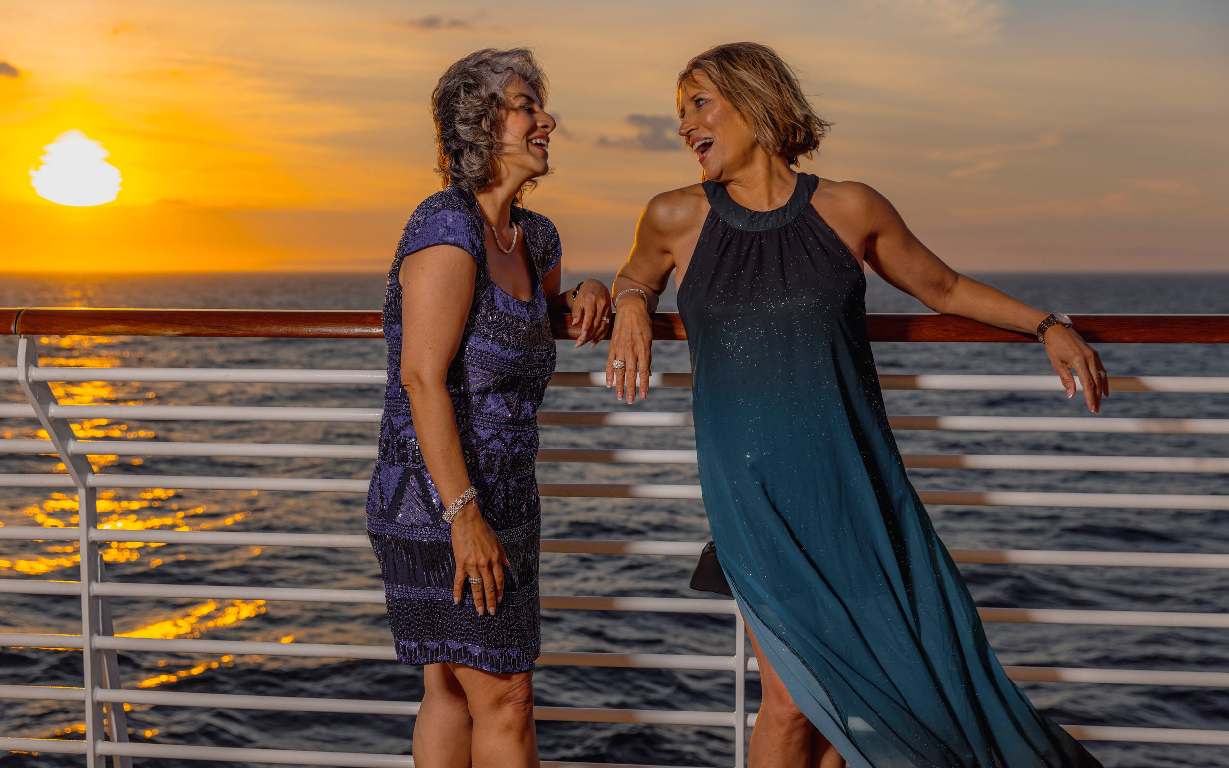 Saga cruise lifestyle photography — two women laughing on deck at sunset, sea behind