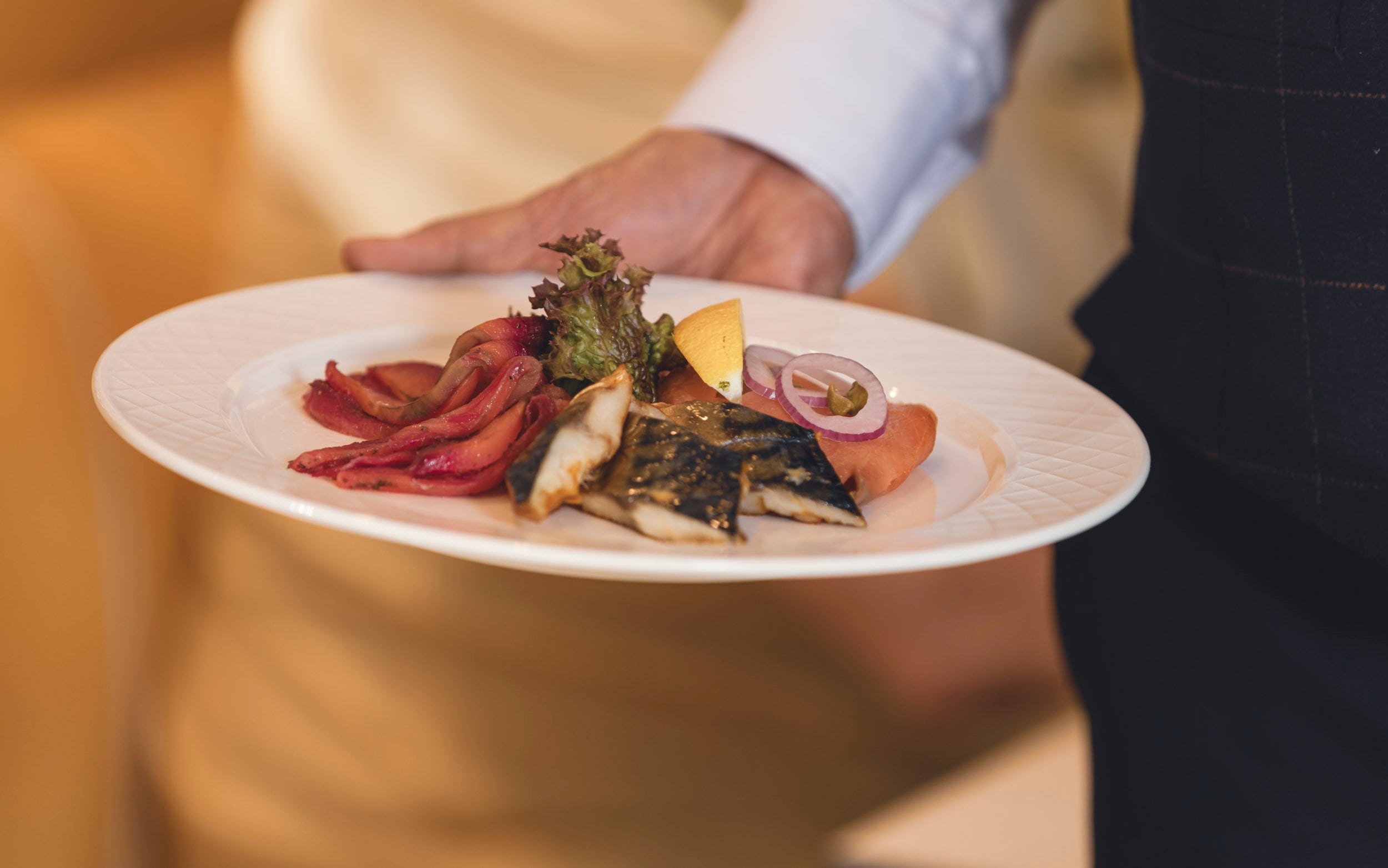 Saga cruise fine-dining photography — plated fish course of mackerel and smoked salmon held by a waiter