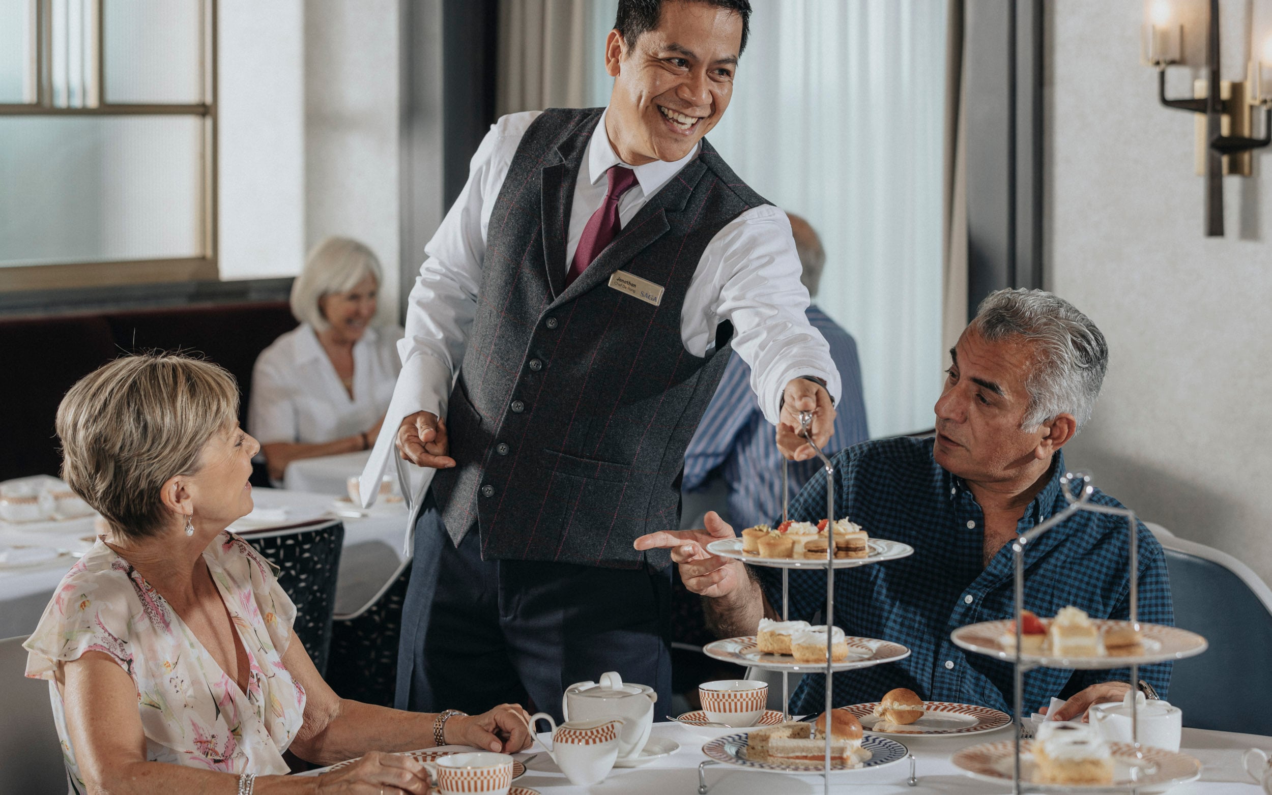 Saga cruise dining photography — afternoon tea service with a tiered cake stand presented to a couple